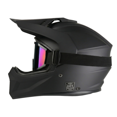 Side profile of a matte black full-face dirt bike or motocross helmet with tinted, iridescent goggles attached over the eye port and a DOT safety certification badge visible near the lower base.